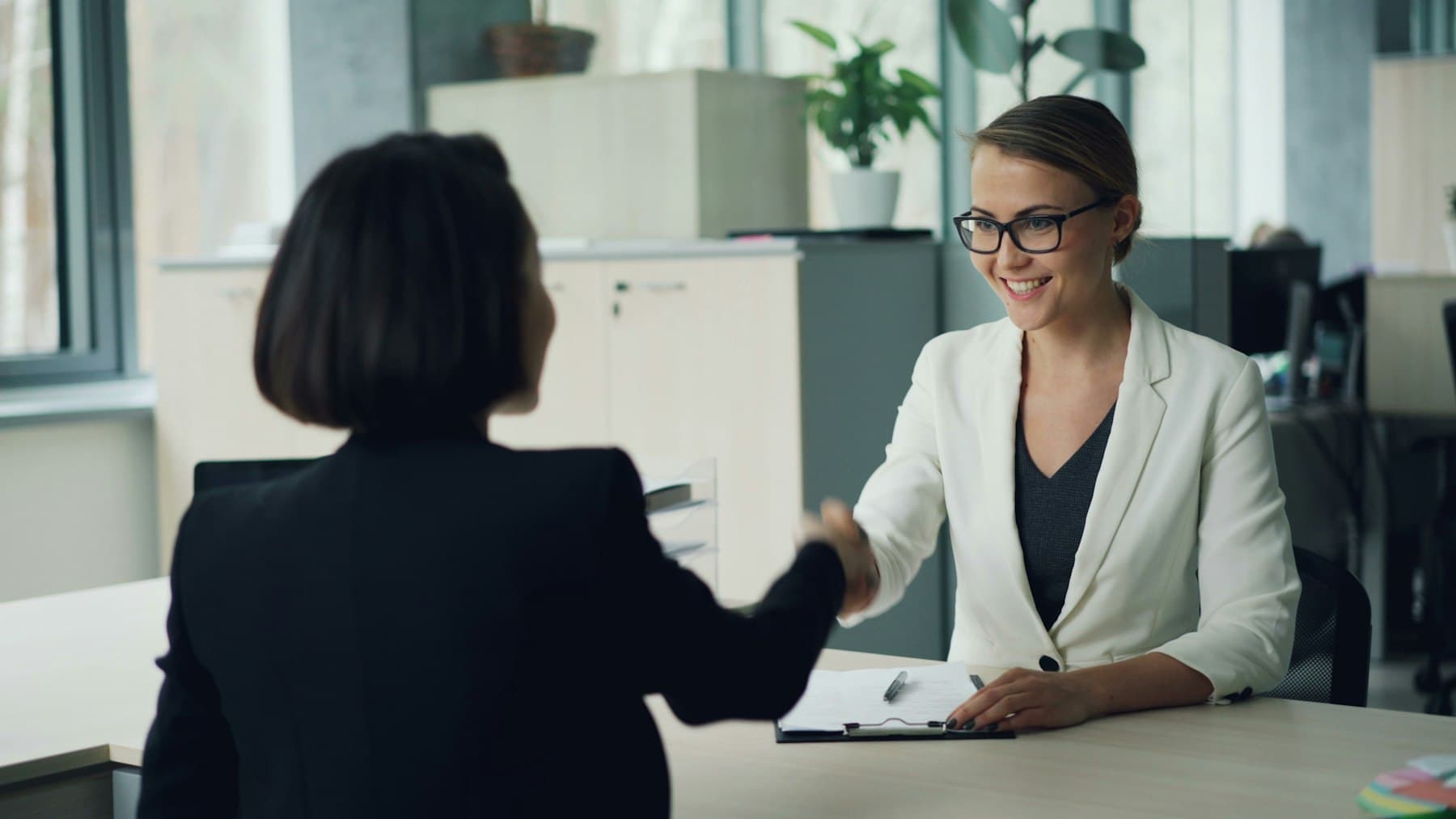 A recruiter and a candidate shaking hands across a desk.